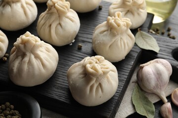 Uncooked khinkalis (dumplings) with peppercorns, garlic and bay leaves on black table, closeup