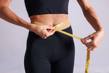 Woman measuring her belly with tape on light grey background, closeup
