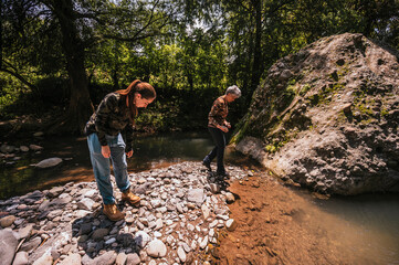 Mother and daughter observing small details like plants, stones, insects, and having a good time by...