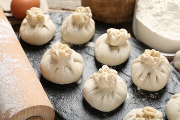 Uncooked khinkalis (dumplings), flour, egg and rolling pin on table, closeup