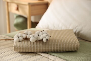 Folded towel and cotton flowers on bed linens at home, closeup