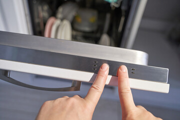 Person adjusts open dishwasher door with control panel in home kitchen interior.