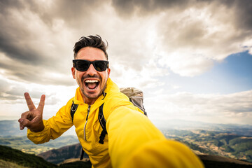Young hiker man taking selfie portrait on the top of mountain - Happy guy smiling at camera -...