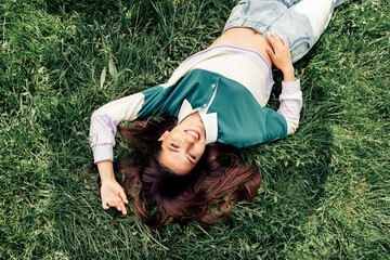 Young woman enjoying outdoors lying on the grass in a casual sweatshirt on a sunny day in a green...