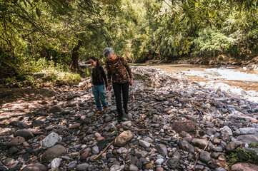 Mother and daughter walking along the riverbank, observing the small details like plants and...