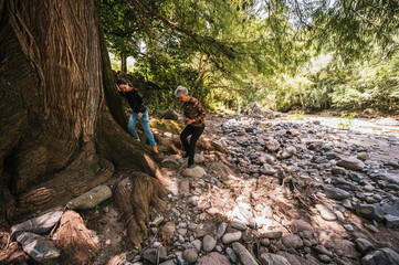 Mother and daughter walking along the riverbank, observing the small details like plants and insects, and having a good time.