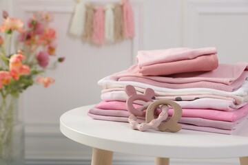 Stack of clean baby clothes and toy on white table indoors, closeup