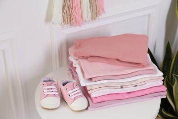 Stack of clean baby clothes and shoes on white table indoors, closeup
