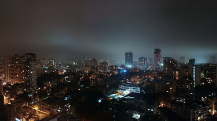 Obraz premium Panoramic nighttime cityscape with illuminated skyline and urban lights under a misty sky 