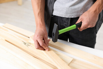 Man hammering nail into wooden plank indoors, closeup