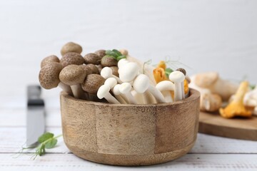 Different raw mushrooms and microgreens in bowl on light wooden table, closeup