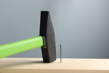 Metal nail in wooden plank and hammer on grey background, closeup