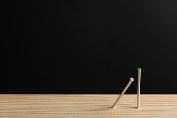 Metal nails in wooden plank against black background, closeup. Space for text