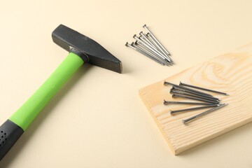 Metal nails, hammer and wooden plank on beige background, above view