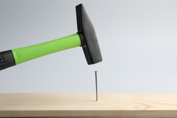 Hammering nail into wooden plank on light grey background, closeup