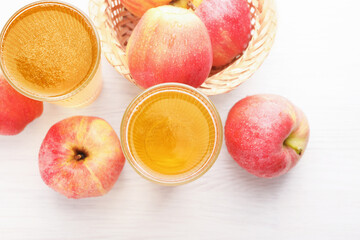 Delicious cider in glasses and red apples on white wooden table, flat lay