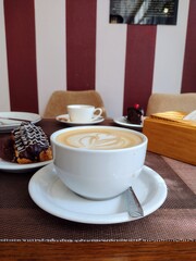 Cup of cappuccino with latte art served with chocolate éclair on plate. Perfect for café advertising, coffee shop menu, bakery promotion, social media food content, lifestyle marketing.