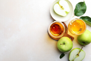 Fresh cider in glasses, apples and green leaves on beige table, flat lay. Space for text