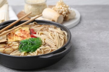 Tasty ramen with enoki and king oyster (eryngii) mushrooms on light grey table, closeup. Space for text