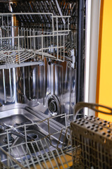 Open built-in dishwasher machine with empty space in modern yellow kitchen. Front view, vertical.