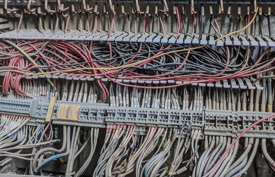 Close-up of tangled electrical wiring and terminal blocks inside an industrial control panel with multiple colored cables.
