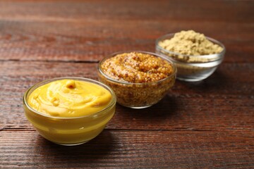 Different types of mustard on wooden table, closeup