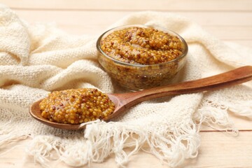 Whole grain mustard in glass bowl and spoon on wooden table, closeup