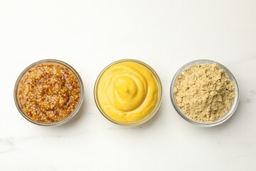 Different types of mustard on white marble table, flat lay