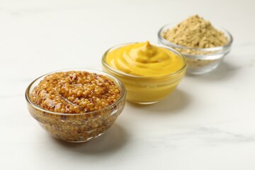 Different types of mustard on white marble table, closeup