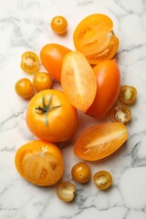 Whole and cut yellow tomatoes on white marble table, flat lay