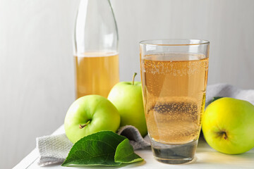 Fresh cider in glass, bottle and apples on white wooden table, closeup