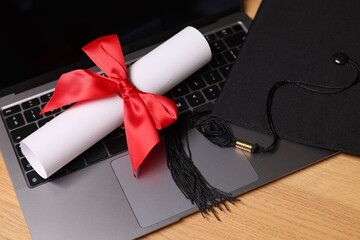 Graduation cap, laptop and diploma on wooden table, closeup