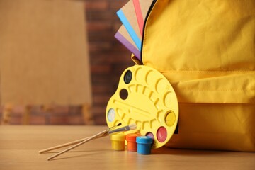 Yellow backpack with notebooks and art supplies on desk in classroom, closeup. Space for text