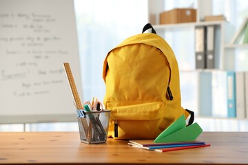 Backpack, different stationery and paper plane on desk in classroom