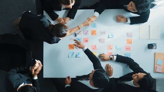 Smart manager looking at board while making handshaking with investor while business group making decision to work together. Diverse marketing team using sticky notes to brainstorm idea. Directorate. - Powered by Adobe