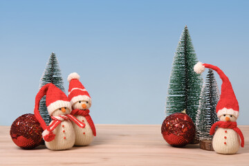 Christmas background with knitted snowmen in red hats and Christmas trees with red ball and space...