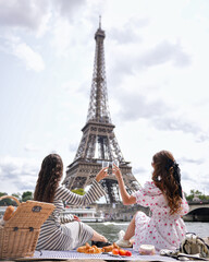 Friends toast with drinks during a relaxed picnic by the Seine River with iconic Eiffel Tower i
