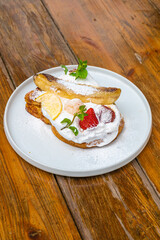 Delicious gourmet dessert with fresh strawberries and banana on a white plate over wood