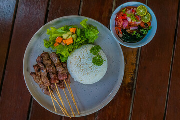 Appetizing Indonesian satay with rice, salad, and vibrant condiments on a wooden table