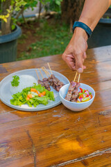 Delicious Indonesian Sate served with rice and fresh vegetables on rustic wooden table