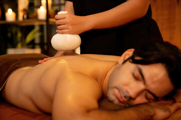 Hot herbal ball spa massage body treatment, masseur gently compresses herb bag on man body....
