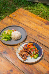 Delicious grilled satay and rice with fresh salad on a rustic wooden table ready to enjoy