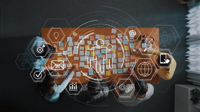 Aerial view of a collaborative workspace featuring team members engaged in brainstorming and planning sessions, utilizing digital technology and sticky notes for idea generation. Raster