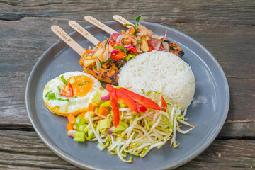 Delicious Indonesian satay skewers with rice, egg, and fresh vegetables on a stylish plate