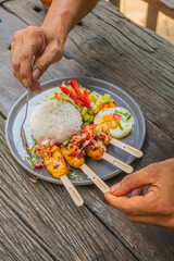 Delicious Indonesian cuisine with rice, skewers, and fresh vegetables on a rustic wooden table