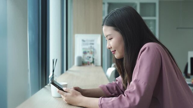 Happy young woman sitting on sofa holding phone smiling enjoying using mobile apps for shopping, having fun playing games, chatting on social media at office