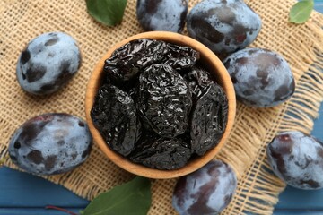Dried prunes and fresh plums on blue wooden table, flat lay