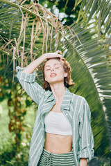 Sunlit portrait of a young woman outdoors, wearing a striped shirt over a white crop top, posing...