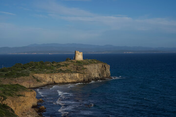 Coastal landscape featuring ancient stone tower on cliffside overlooking serene blue ocean and distant mountains