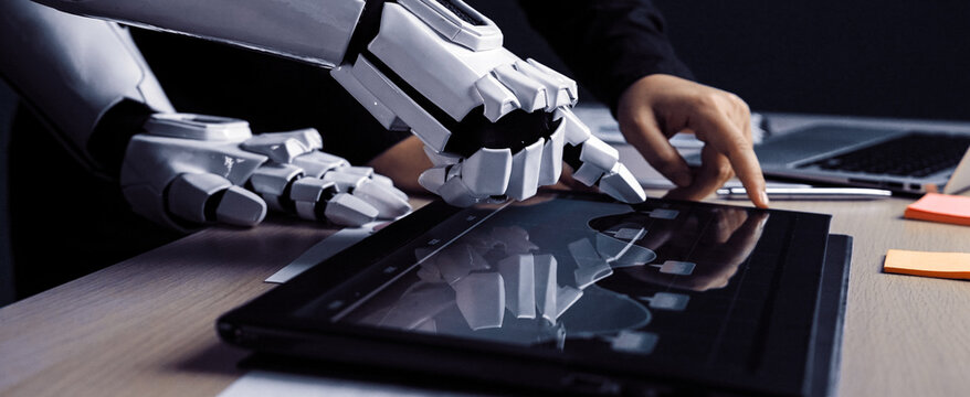 A human hand interacts with a robotic hand on a digital tablet, showcasing a collaboration between technology and human creativity in a modern workspace.Noogenesis